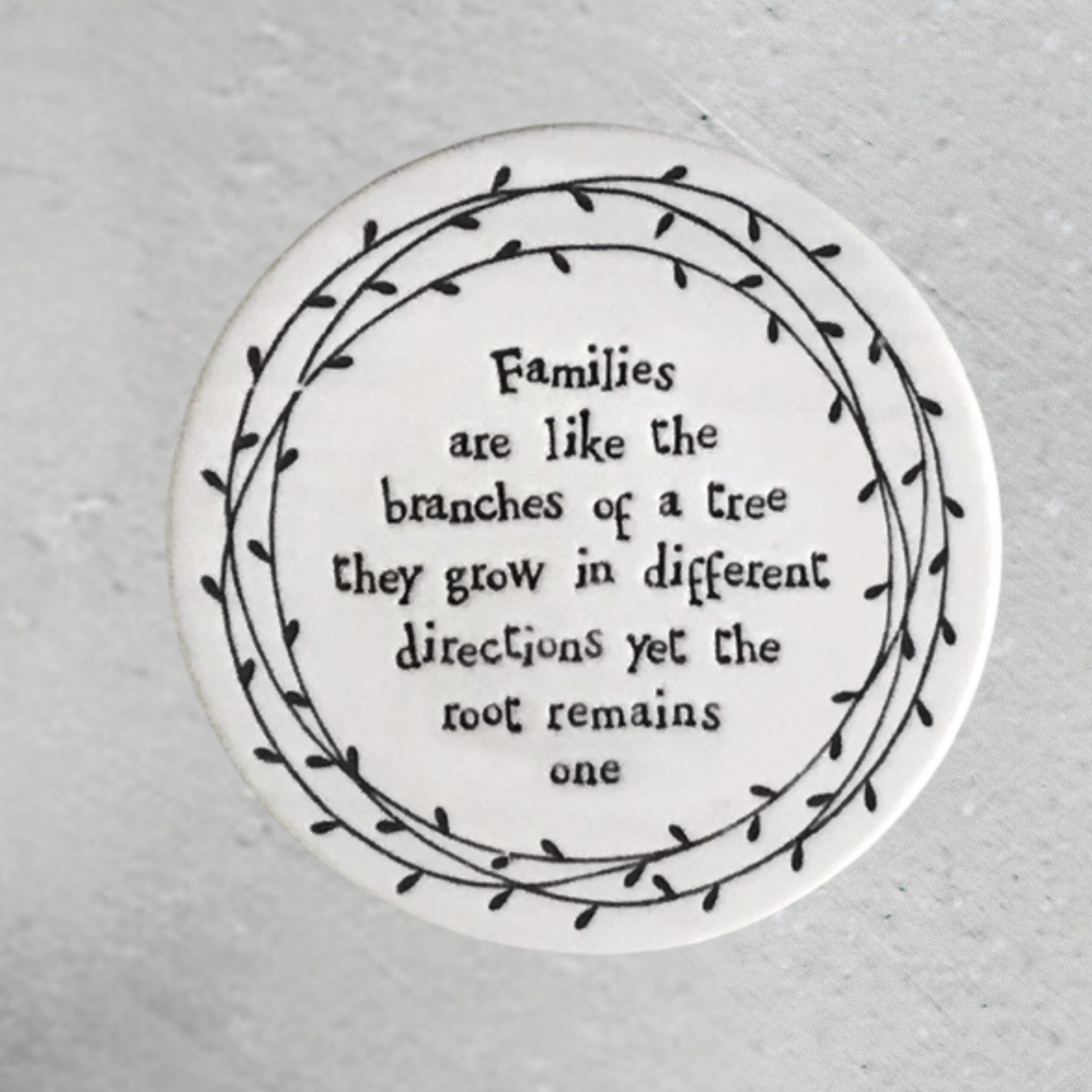 A round porcelain coaster with a black floral pattern and text that reads 'Hope you have an amazing day!' on a textured background.