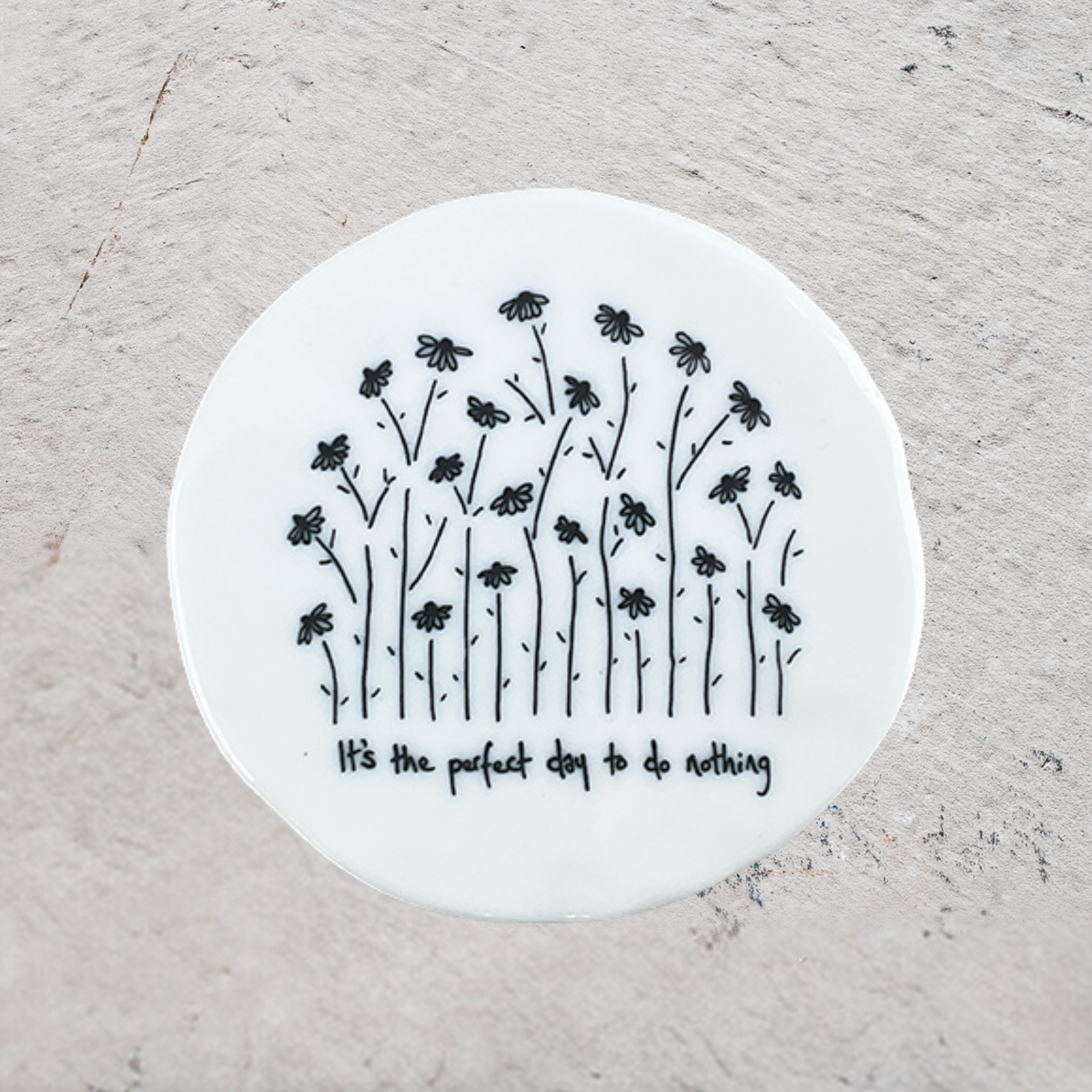 A round porcelain coaster with a black floral pattern and text that reads 'Hope you have an amazing day!' on a textured background.