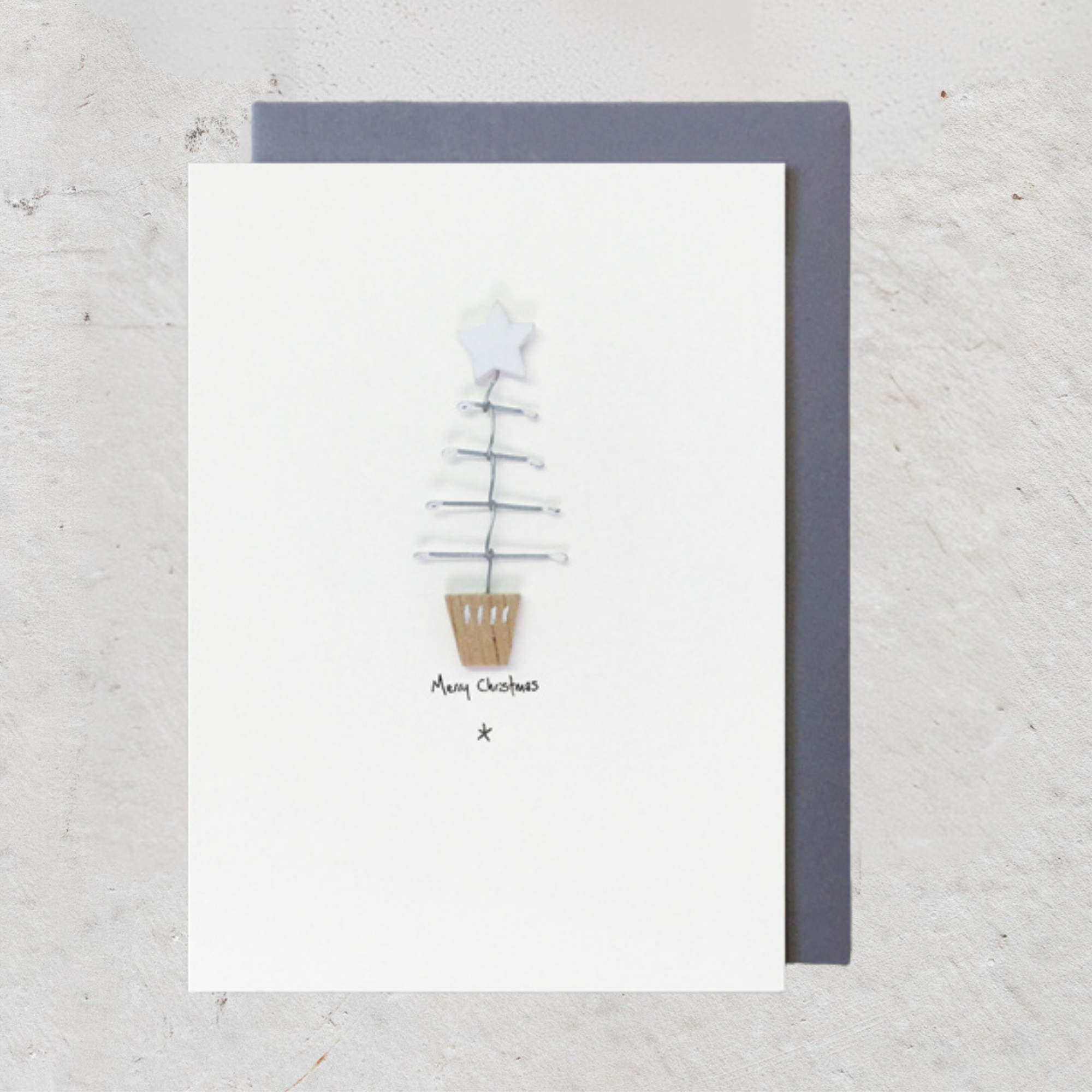 East Of India Woodland Card - Merry Christmas. A contemporary card featuring a wooden Christmas tree with wire branches. Complete with grey envelope, perfect for mailing near or far, and is packaged in a compostable bag, an environmentally friendly choice.
