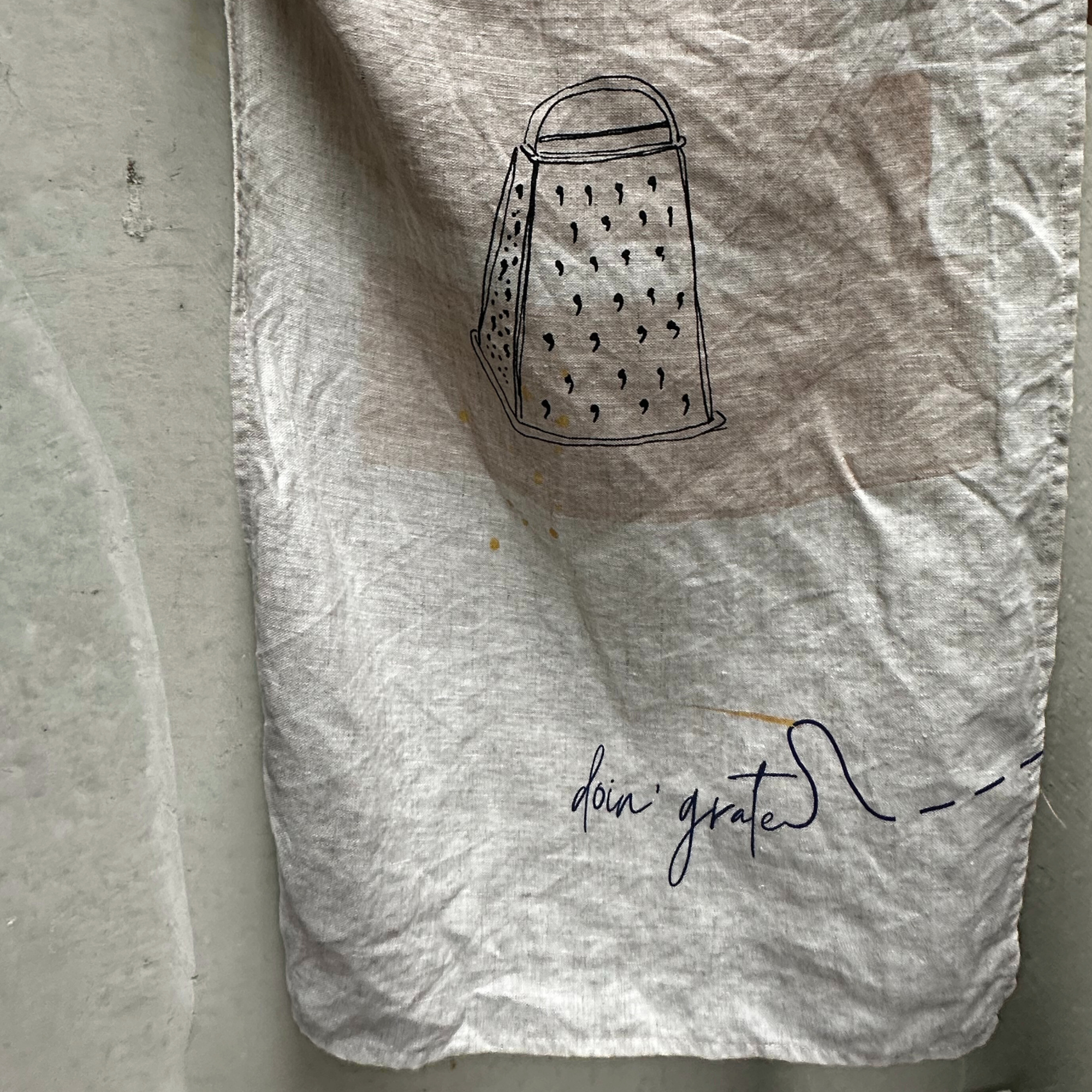 French linen teat towel with a grater graphic and 'doin' grate' text on a plain background
