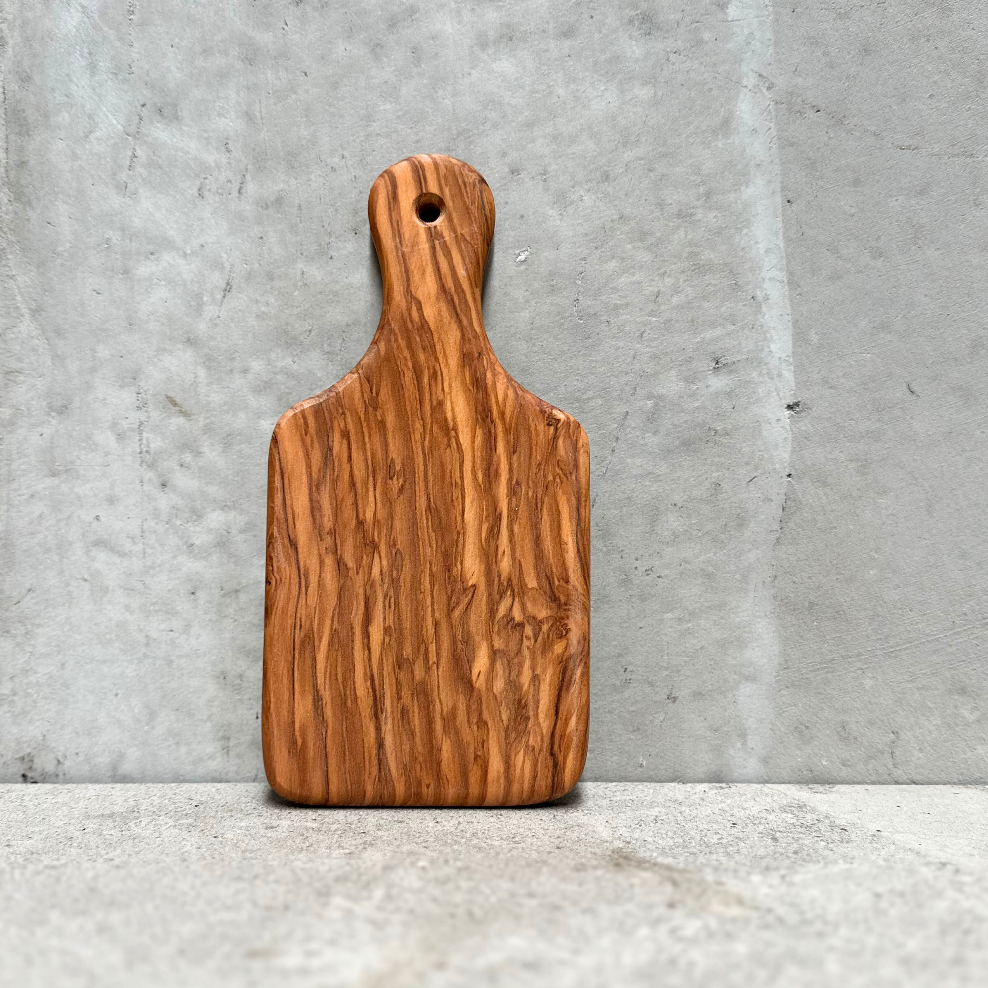 Solid olivewood chopping and serving board with handle, handcrafted in Germany, styled with Brie cheese and potato crisps.