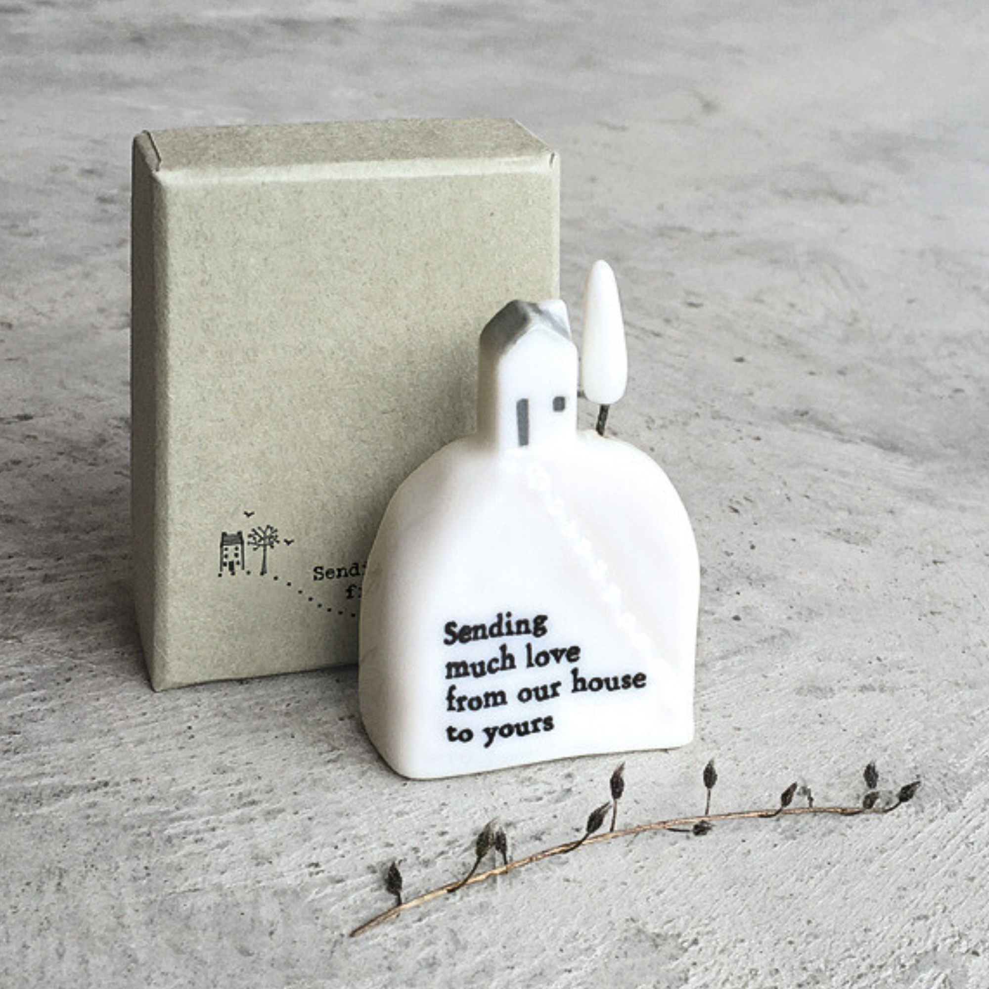 White ceramic  house figurine with text next to a box on a gray surface