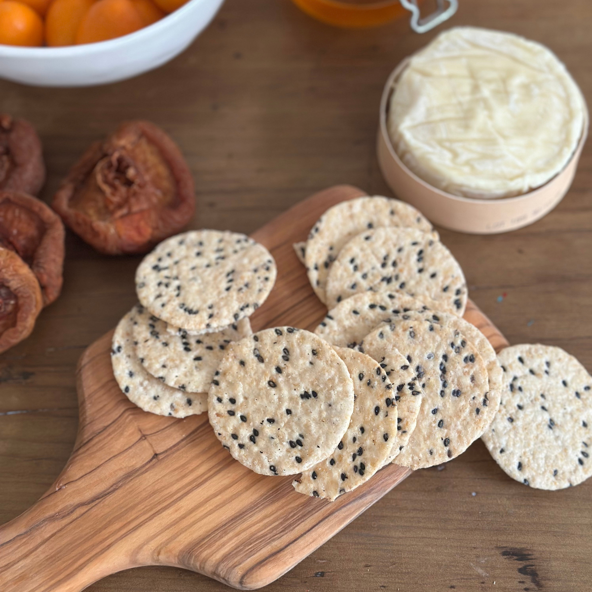 Solid olivewood chopping and serving board with handle, handcrafted in Germany, styled with Brie cheese and potato crisps.