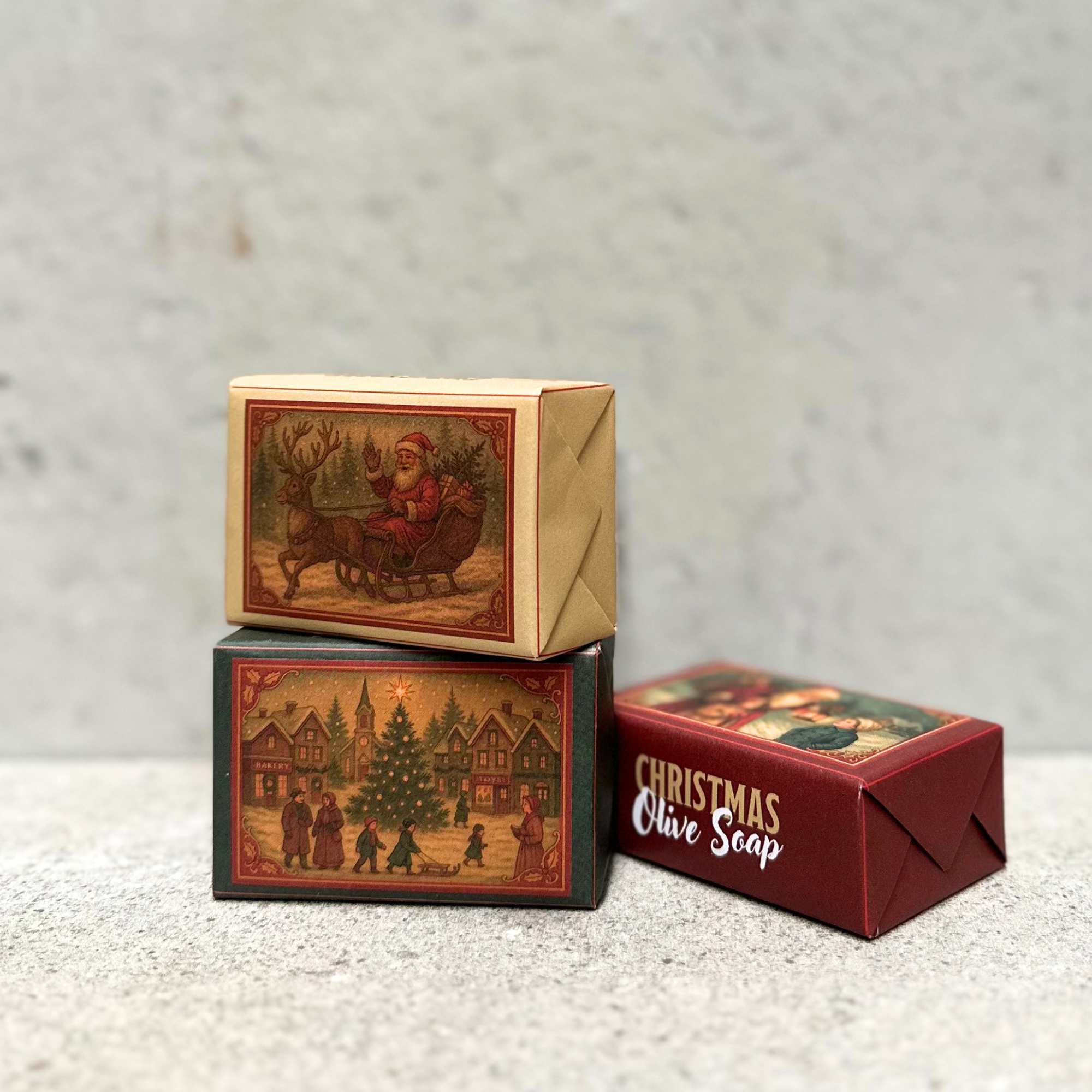 A rectangular green package with a vintage-style Christmas village illustration on the front, placed on a light surface with blurred pine branches and warm string lights in the background.